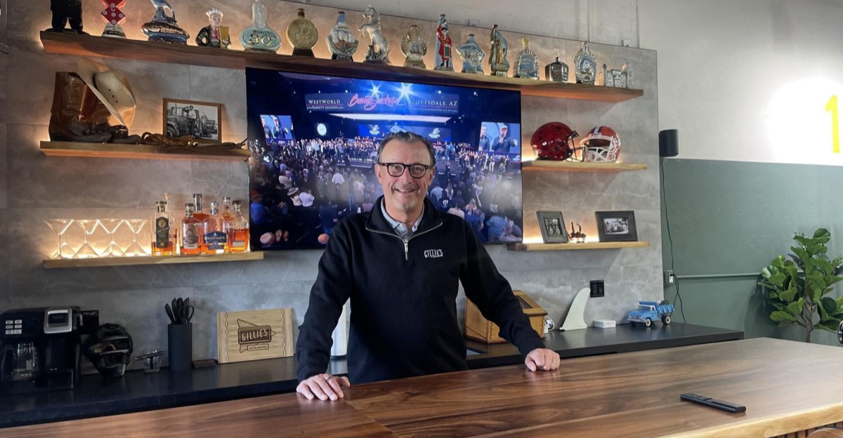 Michael Olguin behind the bar at Gillie's Auto Lounge, with a wall of vintage bourbon bottles and a large-screen TV