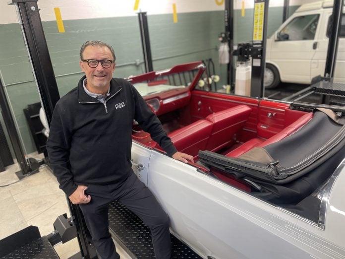 Michael Olguin beside a red-interior classic convertible inside Gillie's Auto Lounge