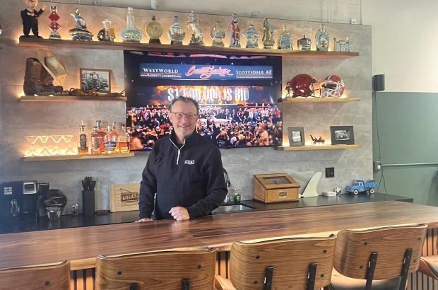 Michael Olguin at the bar at Gillie's Auto Lounge, with a TV and vintage bourbon bottles