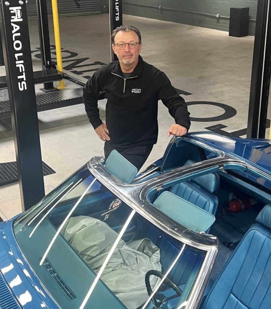 Michael Olguin standing beside a blue classic convertible inside Gillie's Auto Lounge